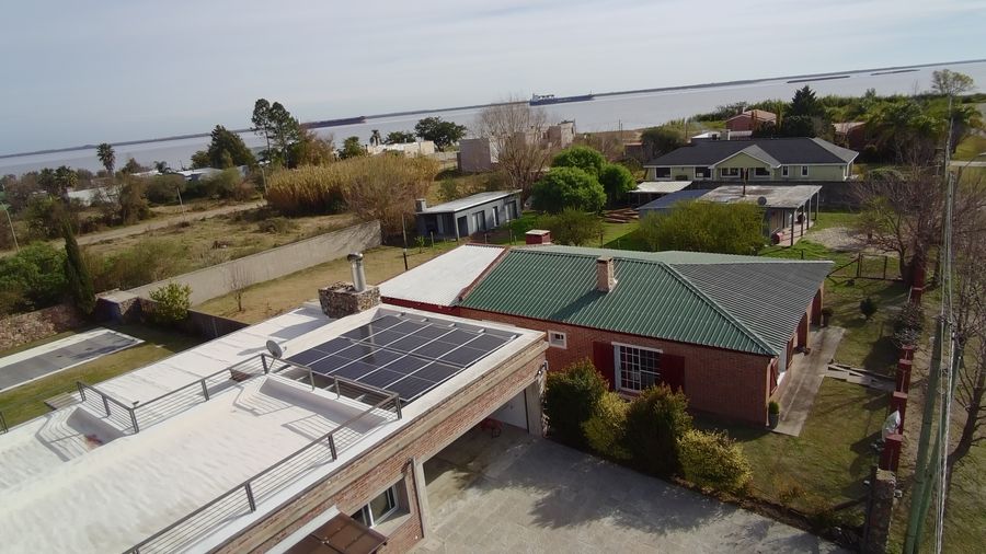Vista aérea de una casa con paneles solares en la azotea y el río de fondo
